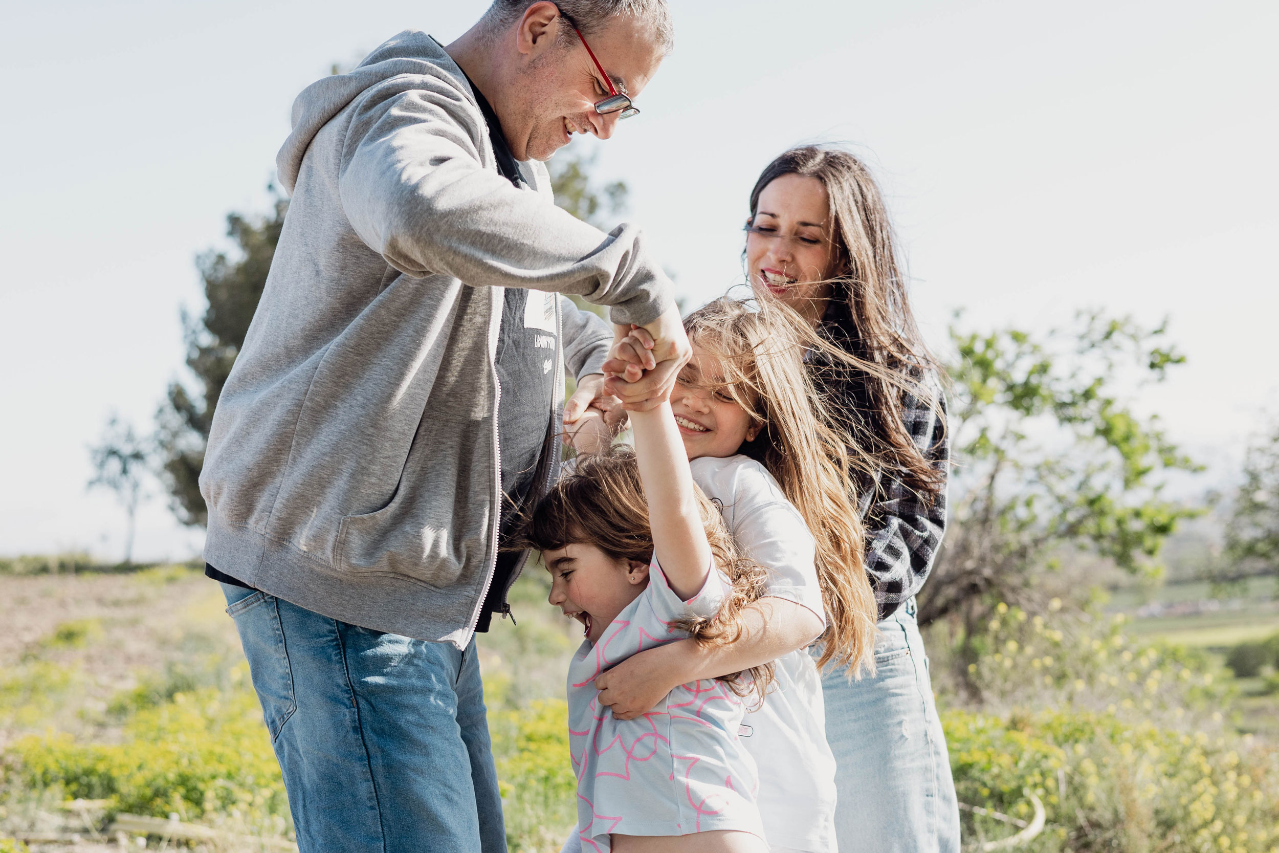 Fotografia de llum natural en família - pares jugant amb les seves filles a l'exterior