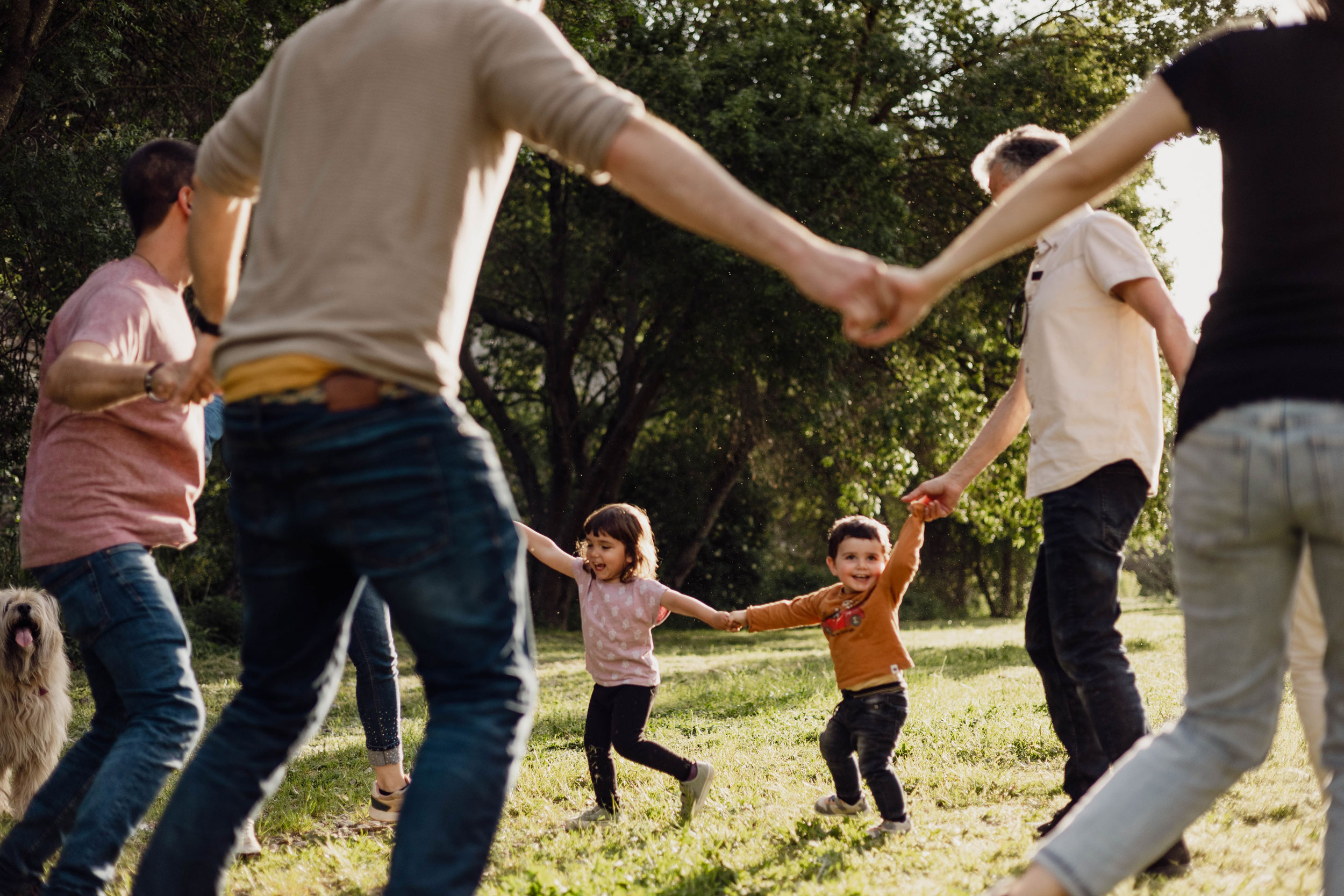 Fotografia de llum natural en família - nens jugant a l'aire lliure agafats de les mans amb adults